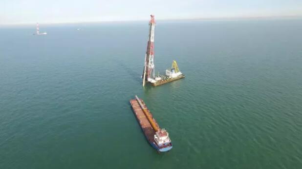 8月22日19點(diǎn)39分，隨著IHC S-800液壓錘的最后一次錘擊，唐山樂亭菩提島海上風(fēng)電場(chǎng)300兆瓦示范工程完成了120根鋼管樁沉樁任務(wù)，提前一天完成了沉樁節(jié)點(diǎn)目標(biāo)。新能源公司承建了本風(fēng)場(chǎng)（B標(biāo)段）的15個(gè)高樁承臺(tái)基礎(chǔ)，每個(gè)承臺(tái)由8根斜度5：1，直徑2米的斜樁組成，鋼樁長(zhǎng)度約為84~89m，樁直徑為2000mm，共120根鋼管樁