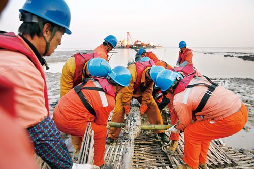 　　“一二三，起！”12月26日上午7點(diǎn)30分，在浙江定海馬目黃金灣水庫(kù)附近淺灘，浙江舟山供電公司220千伏魚(yú)山海纜敷設(shè)工程首根海纜在牽引設(shè)備的牽引下，緩緩進(jìn)入預(yù)設(shè)的電纜溝，成功完成始端登陸，隨即將開(kāi)始為時(shí)60多個(gè)小時(shí)，跨越19.7公里的“跨海”之旅。這也意味著220千伏魚(yú)山輸變電工程項(xiàng)目正式打響了海纜敷設(shè)的“攻堅(jiān)戰(zhàn)”